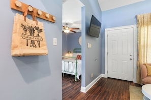 A room with a wooden floor, a white door, a ceiling fan, and a wall-mounted TV.