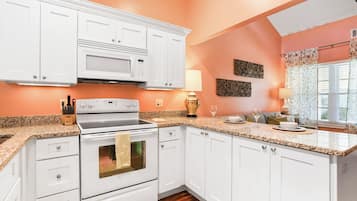 A kitchen with white cabinets, a microwave, and a stove. There is a wooden floor and a window with curtains.