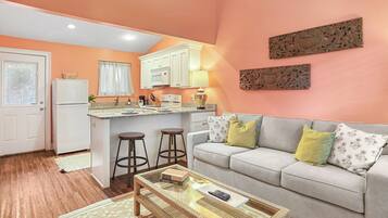 A compact living space with a kitchenette, a sofa with cushions, a coffee table, and a wicker side table.
