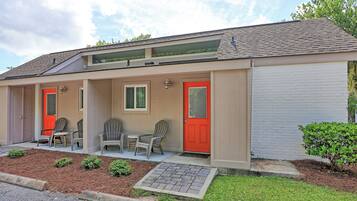 A motel with a covered porch, two red doors, and a small patio area with outdoor seating.