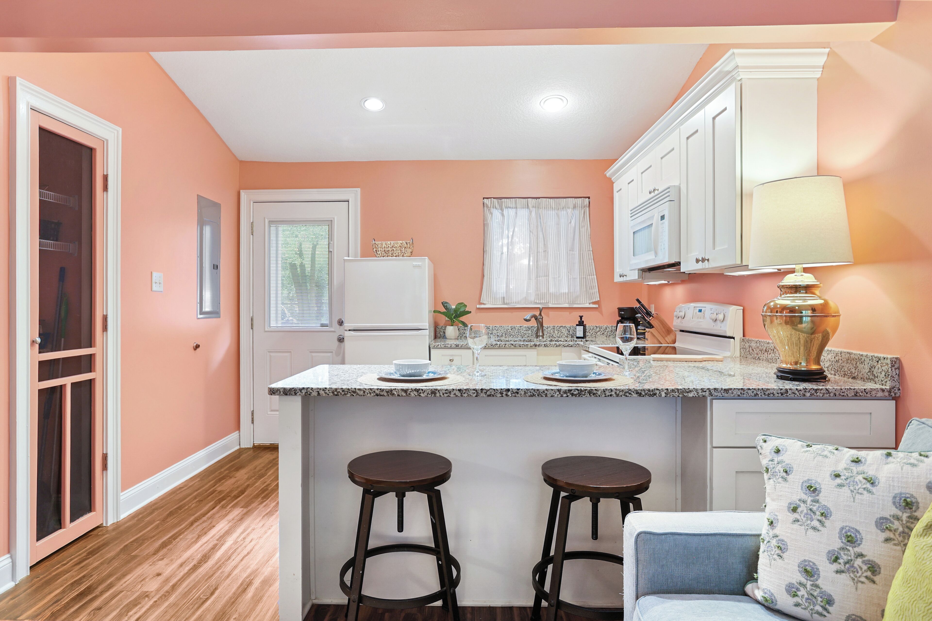 Una cocina con una isla central, taburetes de bar, microondas y estufa.