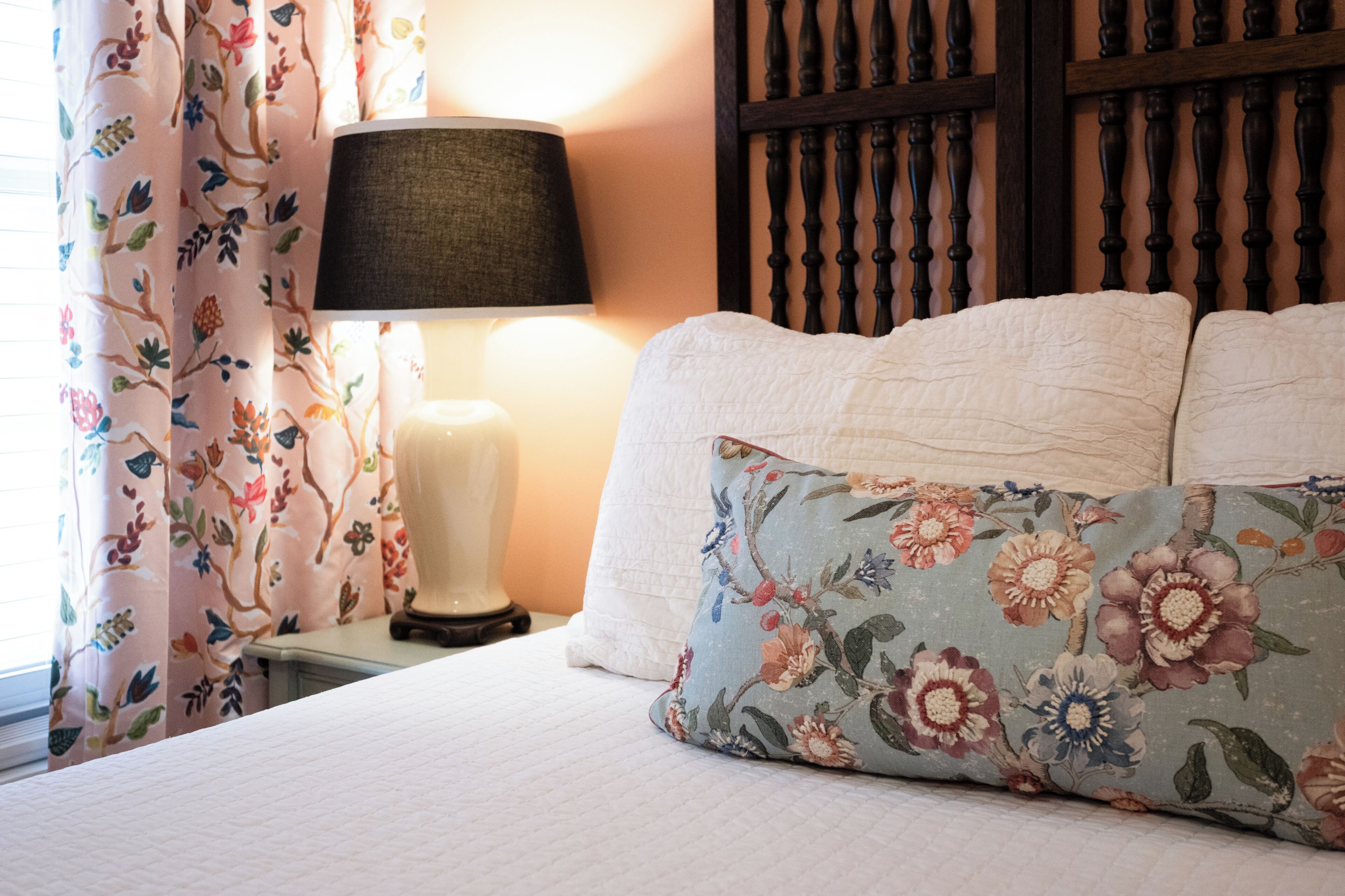 A bed with floral-patterned pillows, a bedside lamp, and a curtain with a floral print.