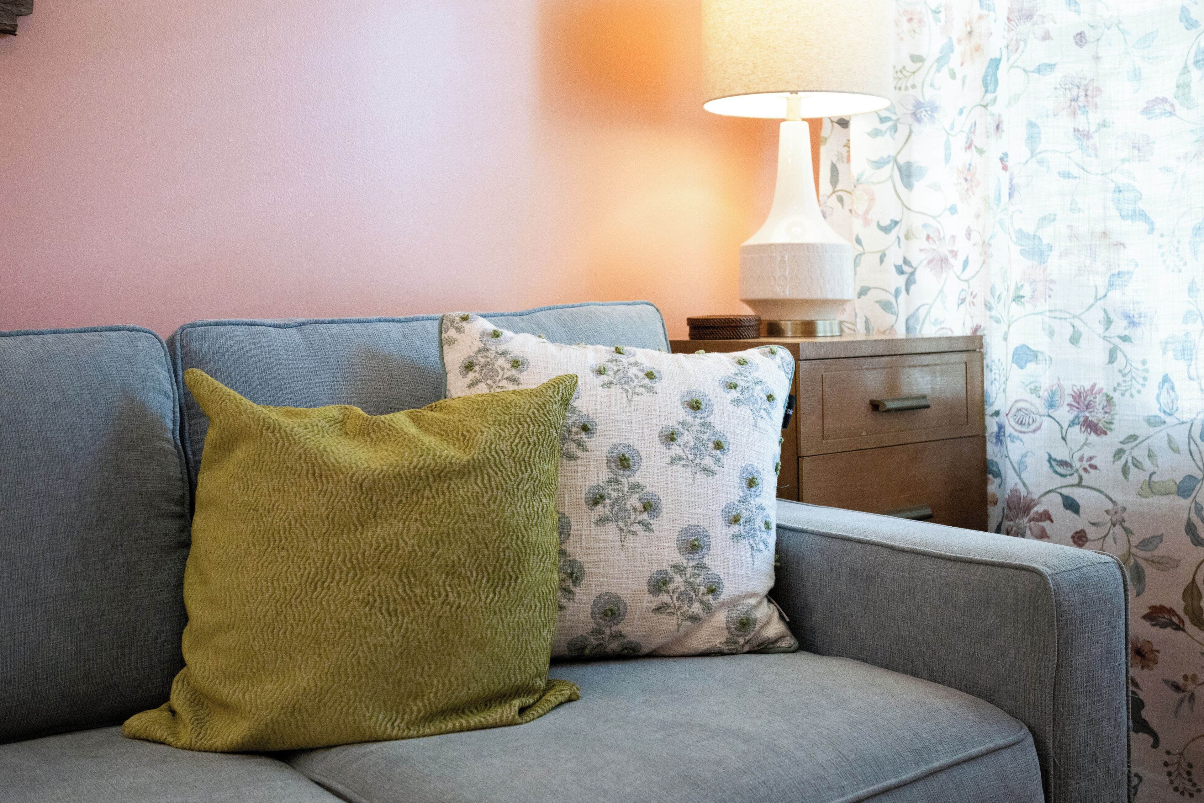 Ein Sofa mit zwei Kissen, einer Lampe und einem blumigen Vorhang.