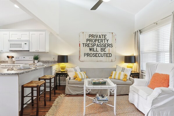 A modern living room with a striped sofa, a coffee table, and a kitchen area with white cabinets and a microwave.