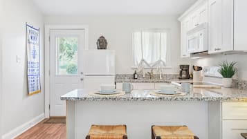 A kitchen with white cabinets, a granite countertop, a refrigerator, a sink, and two stools.