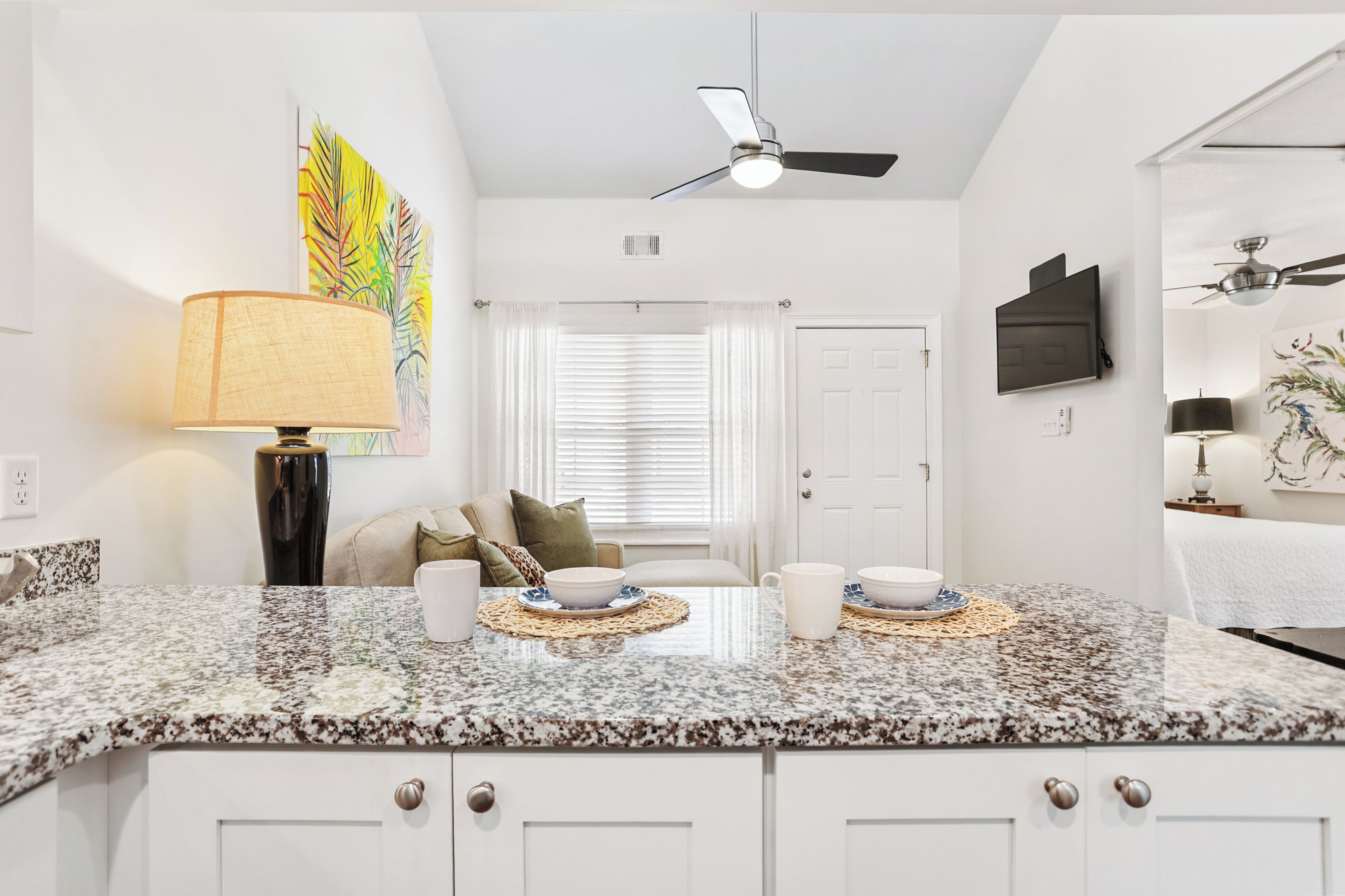 A modern kitchen with granite countertops, white cabinetry, a ceiling fan, and a dining area with a table set for two.