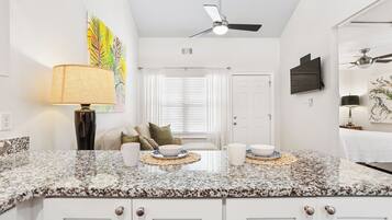 A modern kitchen with granite countertops, white cabinetry, a ceiling fan, and a dining area with a table set for two.