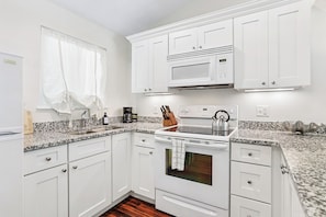 A modern kitchen with white cabinetry, a built-in microwave, a kettle, and a coffee maker. - Cozy Oleander Cottage | Savannah + Tybee l Cohen (Savannah)
