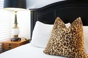 Ein Bett mit einem weißen Kopfkissen und zwei Kissen mit Leopardenmuster, eine Nachttischlampe und ein Nachttisch aus Holz.