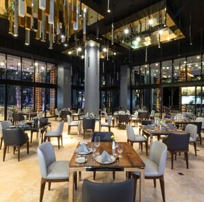 Un intérieur de restaurant moderne, avec de nombreuses tables, des chaises et des luminaires suspendus.