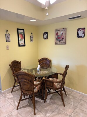 Un'area pranzo con un tavolo in vetro circondato da sedie in vimini, un lampadario a parete e opere d'arte incorniciate.