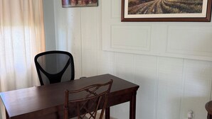 Ein Essbereich mit einem Holztisch und Stühlen, einem Bild an der Wand und einem Fenster mit Vorhängen.
