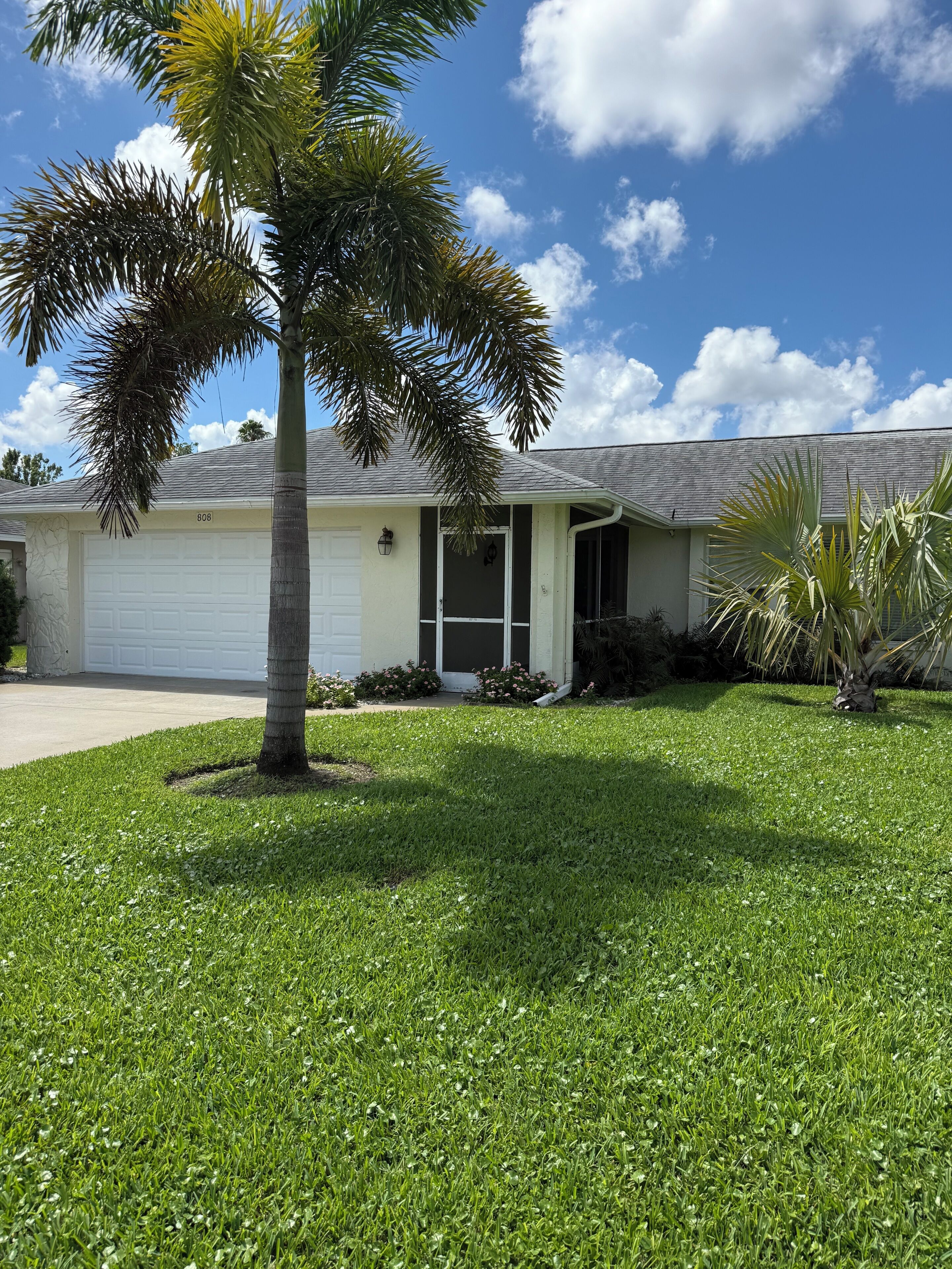 A single-story house with a garage, a lawn, and a palm tree.
