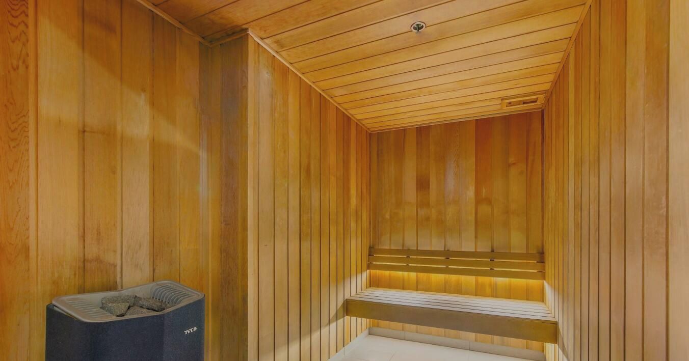 Een sauna met houten wanden en banken, een bankverwarmer en een prullenbak.