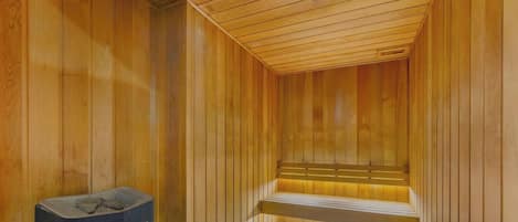 Una sauna con paredes y bancos de madera, un calentador para los bancos y un cubo de basura.