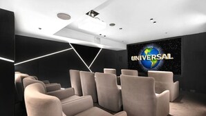 A modern cinema room with rows of plush seating, a large screen displaying the Universal logo, and a geometric light design on the ceiling. - Opulence Oceanview 2BR Suite- The Langham + Parking (Surfers Paradise)