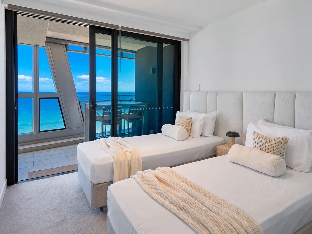 A hotel room with two beds, a view of the ocean, and a balcony with a table and chairs.