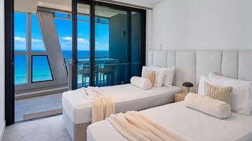 A hotel room with two beds, a view of the ocean, and a balcony with a table and chairs.