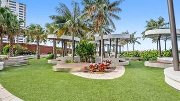 A landscaped outdoor area with palm trees, a circular seating area, and a modern building in the background.