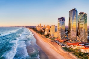 Un paysage urbain côtier avec des immeubles modernes de grande hauteur, une plage de sable et un ciel dégagé.
