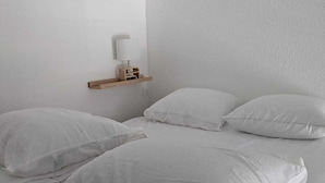 Un dormitorio con cama, almohadas, una mesita de noche y una lámpara de pared.