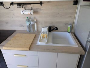 A kitchen with a wooden countertop, a sink, a cutting board, a bottle of water, a bottle of dish soap, and a paper towel holder. - Studio 4 pers Port Cap d'Agde · Plage (Agde)