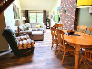 Ein Wohnzimmer mit einer Couch, einem Hocker und einem Esstisch mit Stühlen.