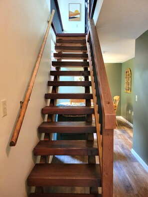 Eine Holztreppe mit Handlauf, die zu einem Zimmer mit einem Bett und einem Fenster führt.