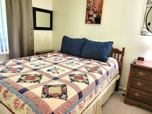 Ein Schlafzimmer mit Bett, Nachttisch, Kommode, Wanduhr und einem Gemälde.