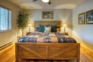 A bedroom with a wooden bed frame, a quilted bedspread, two bedside lamps, a wall-mounted painting, and a potted plant. - Cozy Bear Themed Cabin in Pinetop Country Club (Pinetop Country Club)