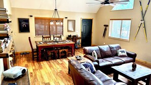 A spacious living room with a large leather sofa, a dining table with chairs, a ceiling fan, and a projector on the floor. - Cozy Bear Themed Cabin in Pinetop Country Club (Pinetop Country Club)