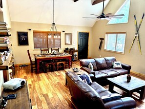 A spacious living room with a large leather sofa, a dining table with chairs, a ceiling fan, and a projector on the floor. - Cozy Bear Themed Cabin in Pinetop Country Club (Pinetop Country Club)