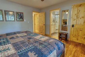 A bedroom with a large bed, wooden doors, a small stool, and a bathroom visible through an open door. - Cozy Bear Themed Cabin in Pinetop Country Club (Pinetop Country Club)