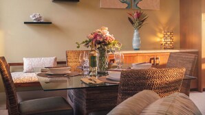 A dining area with a glass table, wicker chairs, a vase of flowers, and a painting on the wall. - Fall $250 Wailea Luxury Escape.Ocean & Haleakala Views.1 Bed/ 2 Bath.Huge Lanai! (Wailea)