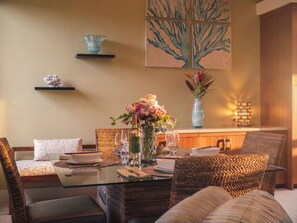 A dining area with a glass table, wicker chairs, a vase of flowers, and a painting on the wall. - Fall $250 Wailea Luxury Escape.Ocean & Haleakala Views.1 Bed/ 2 Bath.Huge Lanai! (Wailea)