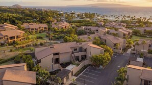 A residential area with multiple two-story buildings, a parking lot, and a view of the ocean. - Fall $250 Wailea Luxury Escape.Ocean & Haleakala Views.1 Bed/ 2 Bath.Huge Lanai! (Wailea)