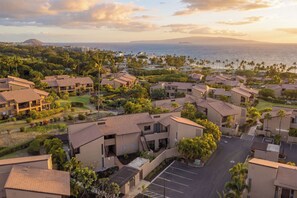 A residential area with multiple two-story buildings, a parking lot, and a view of the ocean. - Fall $250 Wailea Luxury Escape.Ocean & Haleakala Views.1 Bed/ 2 Bath.Huge Lanai! (Wailea)