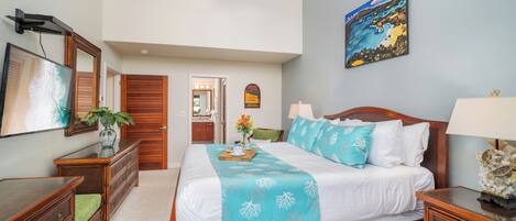 Quarto com cama, mesas de cabeceira, ventoinha no teto, um quadro e vista para o banheiro.