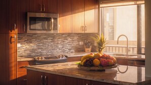 A modern kitchen with wooden cabinets, a stainless steel microwave, a tiled backsplash, and a fruit bowl on the counter. - Fall $250 Wailea Luxury Escape.Ocean & Haleakala Views.1 Bed/ 2 Bath.Huge Lanai! (Wailea)