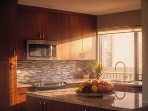 A modern kitchen with wooden cabinets, a stainless steel microwave, a tiled backsplash, and a fruit bowl on the counter. - Fall $250 Wailea Luxury Escape.Ocean & Haleakala Views.1 Bed/ 2 Bath.Huge Lanai! (Wailea)