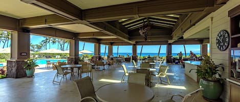 A spacious outdoor patio with multiple tables and chairs, overlooking a pool and the ocean.