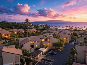 A coastal residential area with houses, a parking lot, and a view of the ocean at sunset. - REMAINING 2026 $200/nt! Luxury!Ocean & Haleakala Views.1 Bed/ 2 Bath.Huge Lanai! (Wailea)