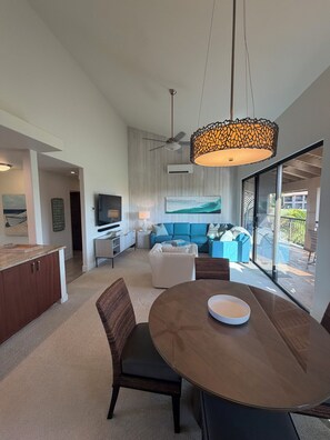 A modern living room with a blue sofa, a dining table with a bowl, and a ceiling fan. - REMAINING 2026 $200/nt! Luxury!Ocean & Haleakala Views.1 Bed/ 2 Bath.Huge Lanai! (Wailea)