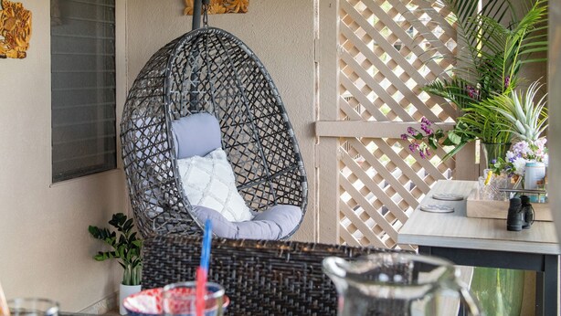 A hanging chair with cushions, a table with a pitcher and glasses, and a lattice screen with plants. - Fall $250 Wailea Luxury Escape.Ocean & Haleakala Views.1 Bed/ 2 Bath.Huge Lanai! (Wailea)