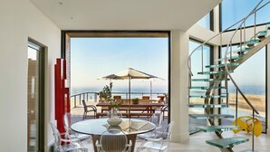 A modern interior with a dining area, clear chairs, a round table, and a view of the ocean. - Iconic Fire Island Pines Oceanfront | Pool, Hot Tub & Sauna (Sayville)