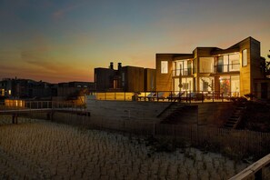 A modern building with a large glass facade, a wooden deck, and a staircase leading to the entrance.