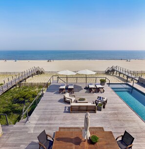 A wooden deck with lounge chairs and a pool, overlooking a beach.