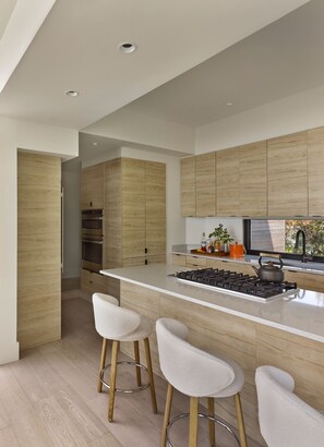 A modern kitchen with wooden cabinetry, a central island with stools, and built-in appliances.