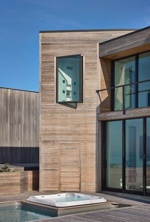 A modern building with a wooden exterior, a glass door, and a hot tub in the foreground.