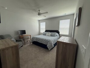 Une chambre à coucher comprenant un lit, un bureau, une chaise, un ventilateur de plafond et deux fenêtres.